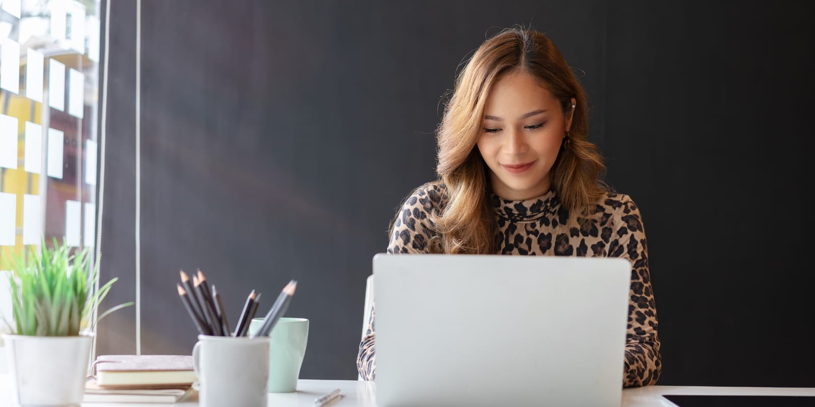 A woman at a laptop by a window, reading what is on the screen before she replies to it