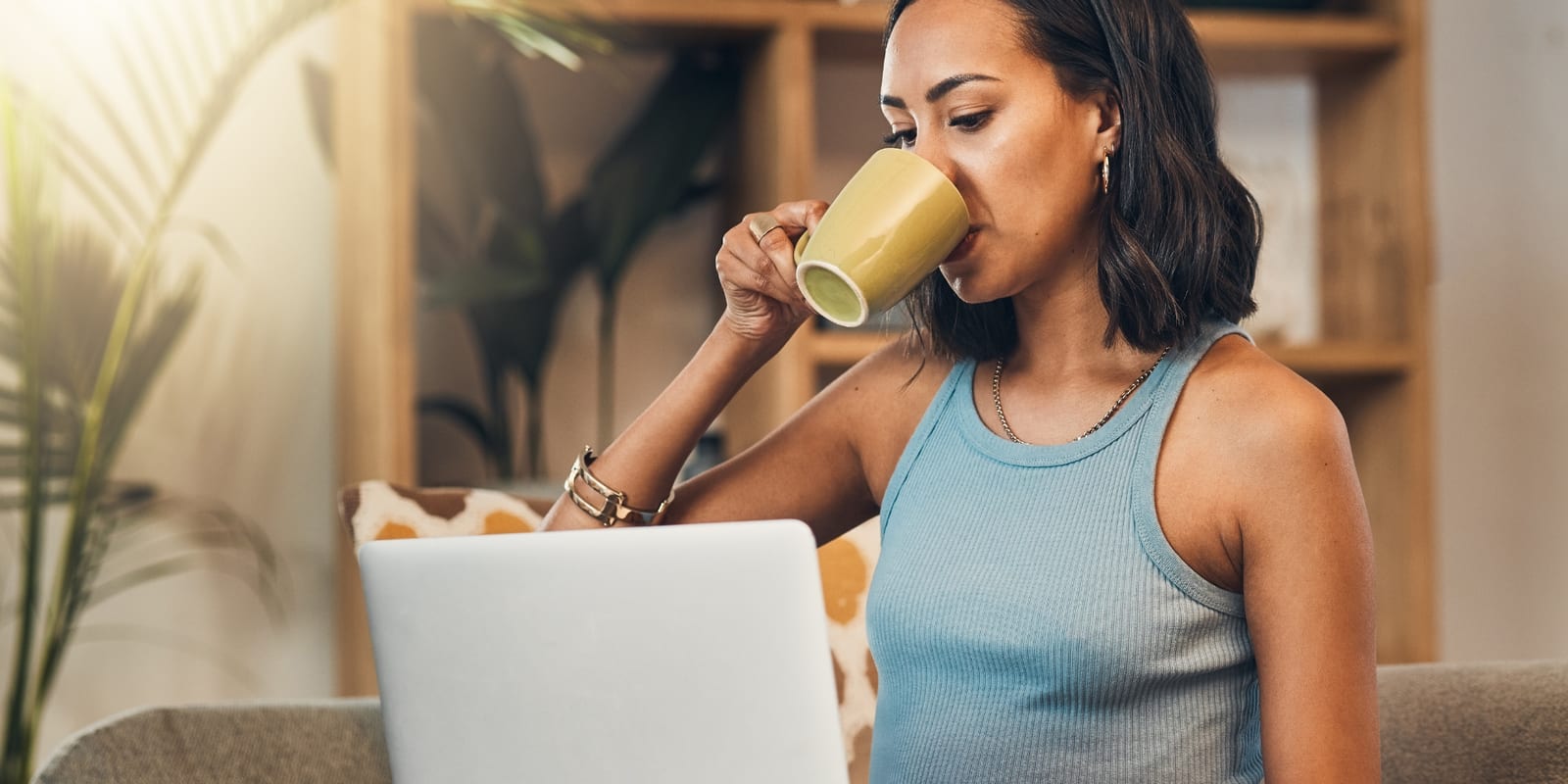 An operator pausing over a coffee in a sunlit room, reading her laptop screen before deciding how to reply